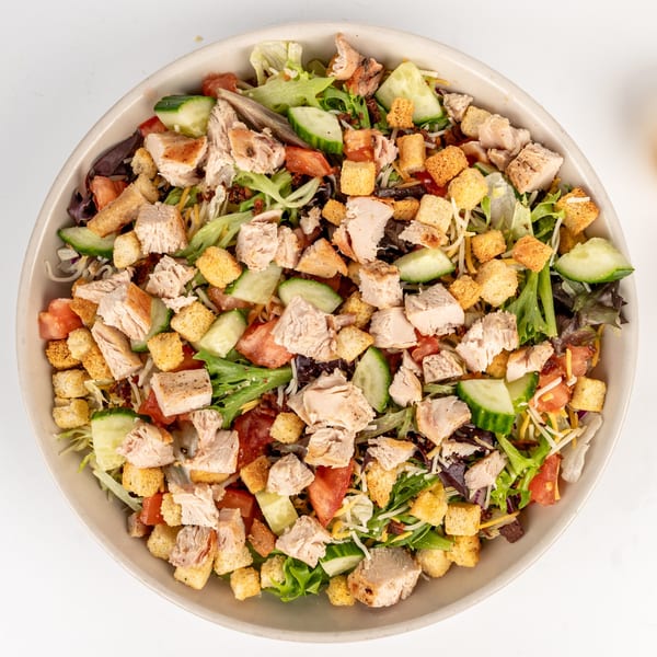Overhead view of a large salad with chicken, croutons, cucumbers, tomatoes, and mixed greens.