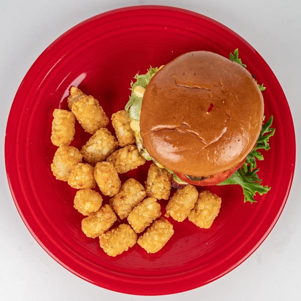 Cheers Sports Eatery burger with lettuce, tomato, and cheese, served with tater tots on a red plate.