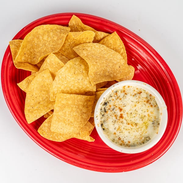 A red oval plate filled with tortilla chips and a side of cheesy spinach dip.