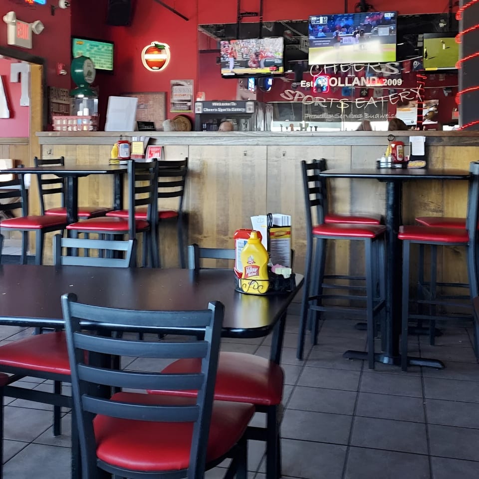 Interior of Cheers Sports Eatery with red walls, TVs showing sports, and black tables with red chairs.