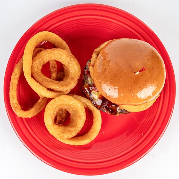 Cheers Sports Eatery's BBQ burger with melted cheese and onion rings on a red plate.