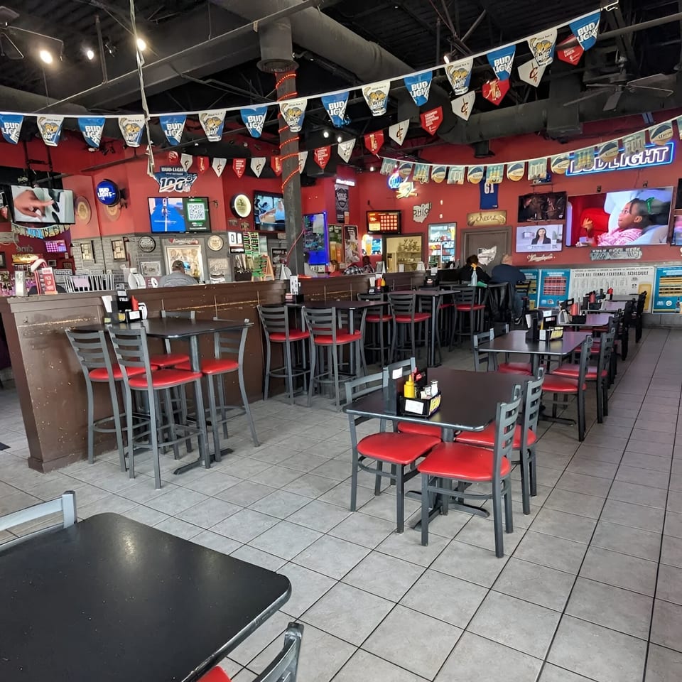 Interior of Cheers Sports Eatery with red walls, multiple TVs, and red and black tables and chairs.