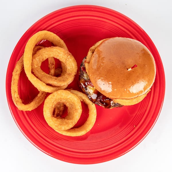 Cheers Sports Eatery burger with BBQ sauce and melted cheese, served with crispy onion rings on a red plate.