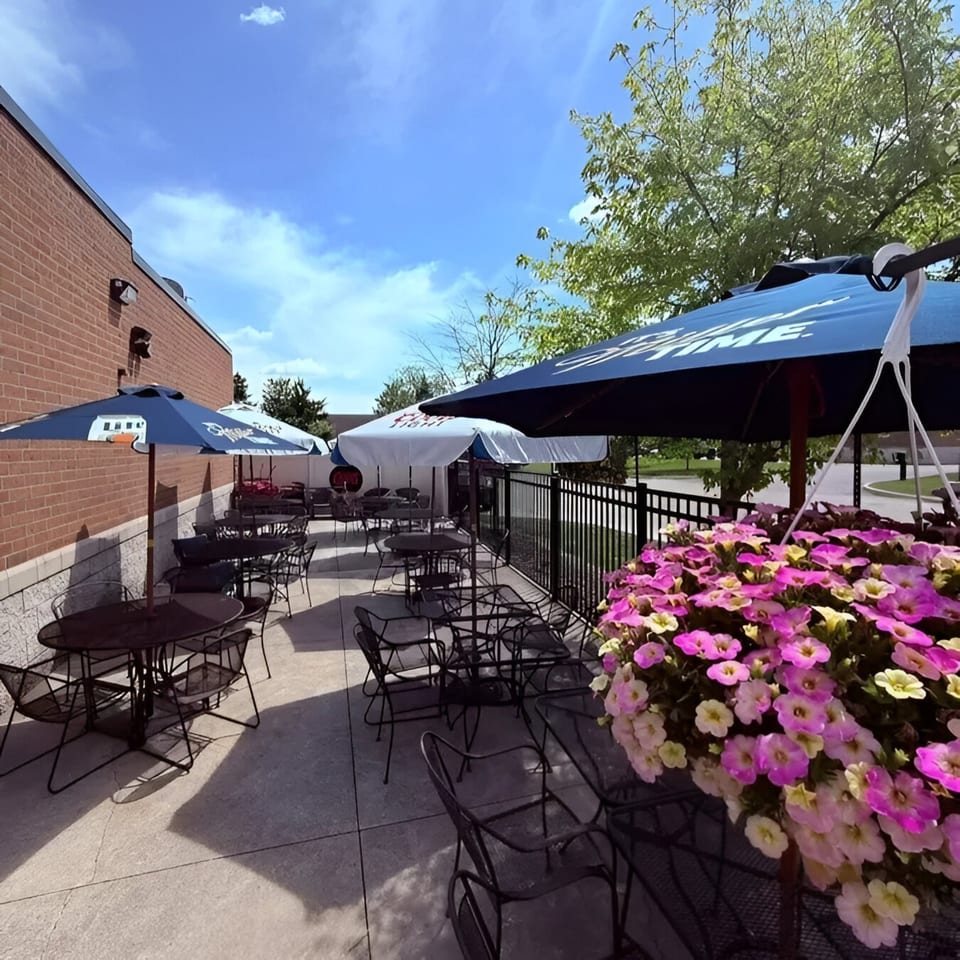 Cheers Sports Eatery's outdoor patio with tables, chairs, umbrellas, and hanging flower baskets.