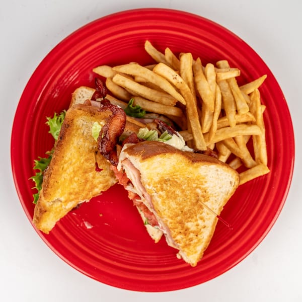 Cheers Sports Eatery's club sandwich with bacon, lettuce, tomato, and fries on a red plate.